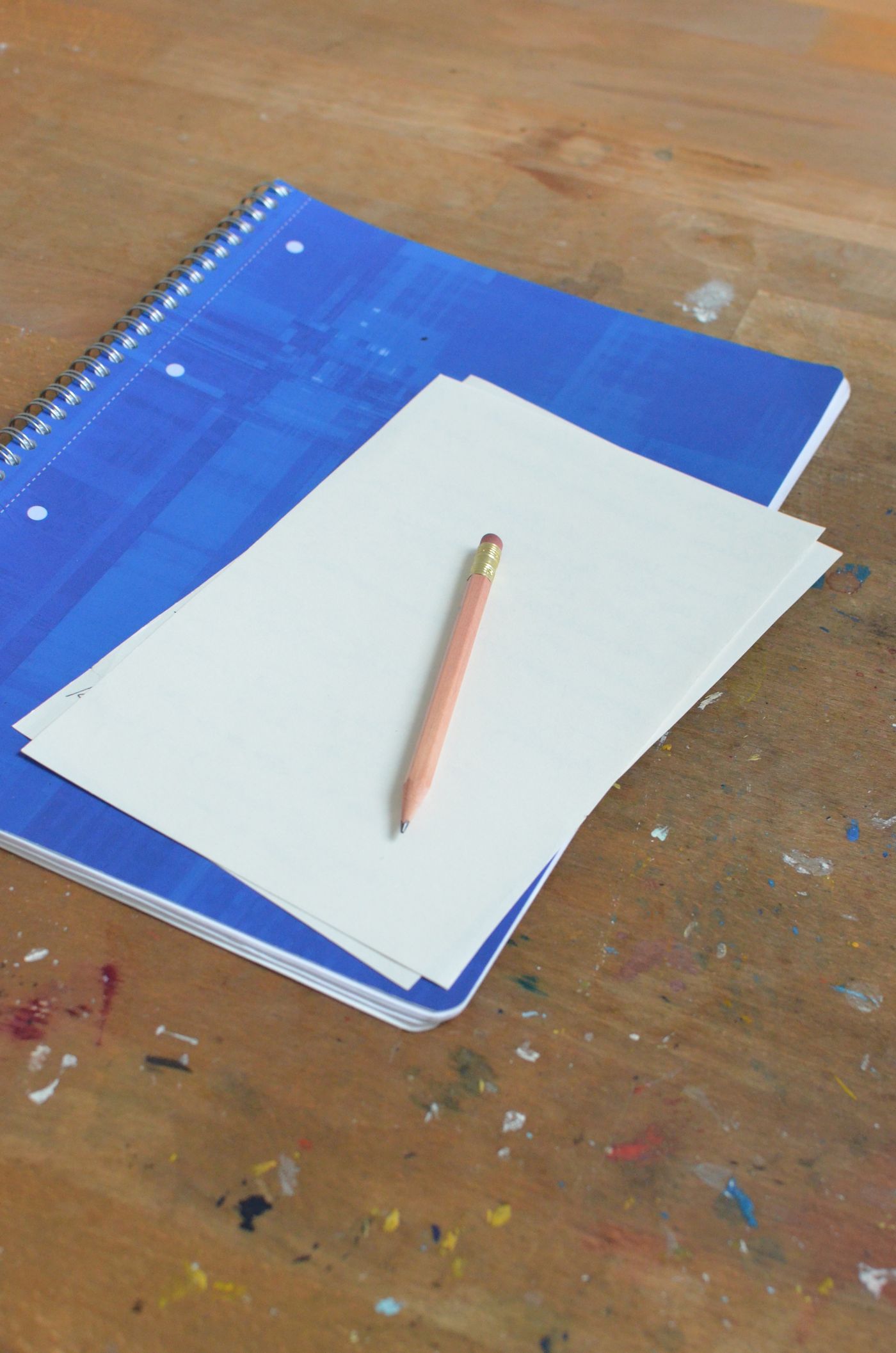Blank notebook pages and a pencil on a wooden desk.