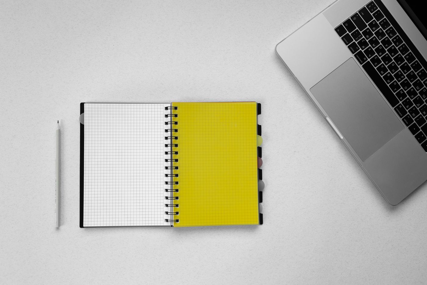 A pencil and open grid notebook beside a laptop.